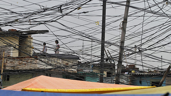 Tangled overhead electric power cables are pictured at a residential area as children stand on the roof of a house in Noida